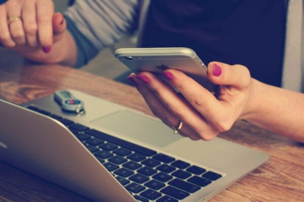a woman holding a mobile device near a laptop.